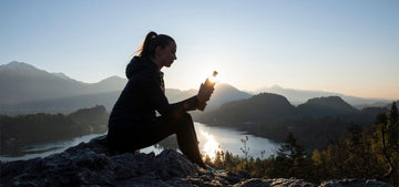 mädchen auf dem berggipfel sitzend mit glasflasche mit flaska trinkflasche in der hand