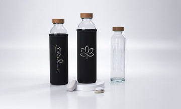 drei glas trinkflaschen mit schwarzen hüllen und holzdeckeln zwei haben minimalistische designs