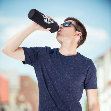 junge in blauem t-shirt trinkt aus glasflasche flaska mit schwarzer neoprenhülle und tangram design