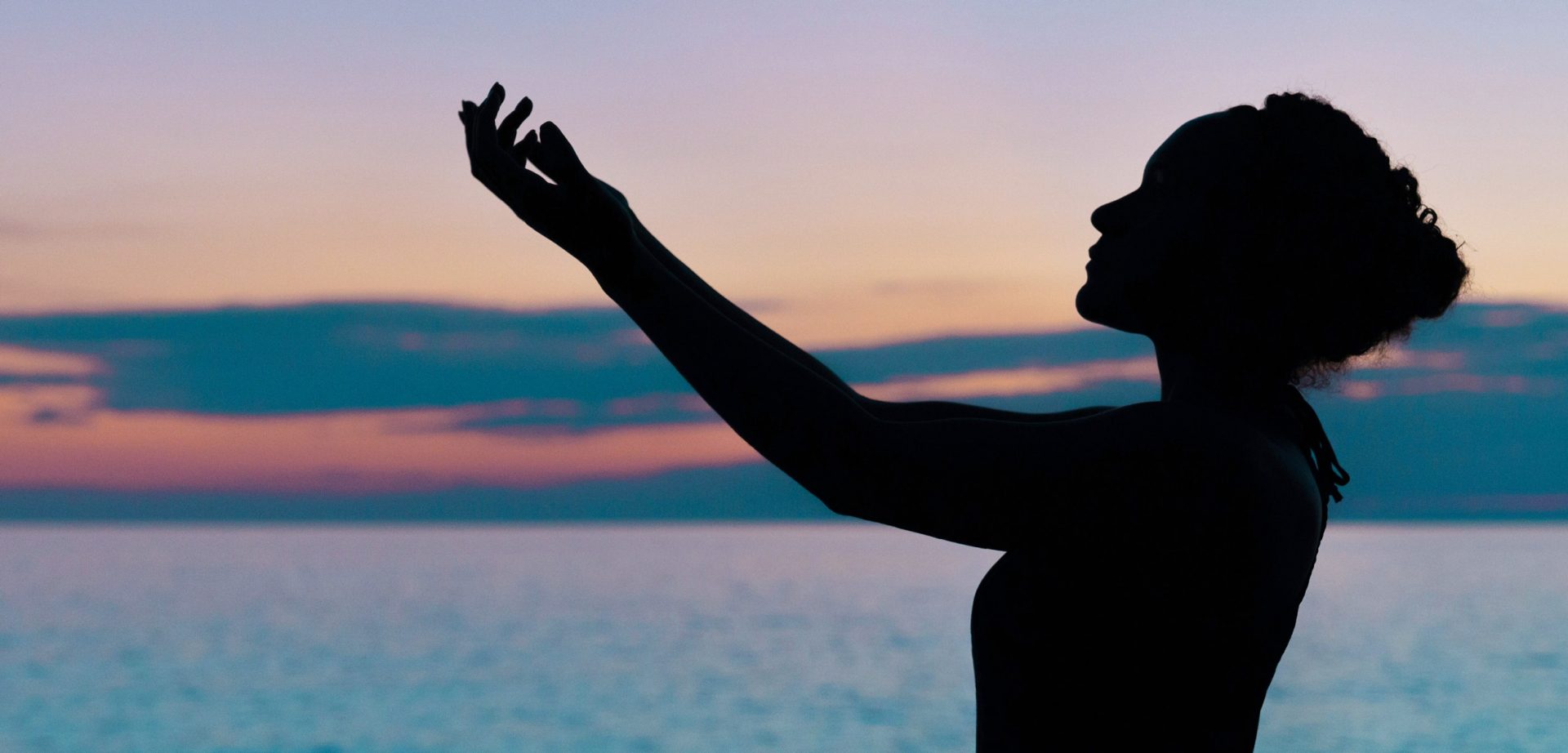 silhouette einer frau, die dem sonnenuntergang entgegenblickt arm in friedvoller pose erhoben