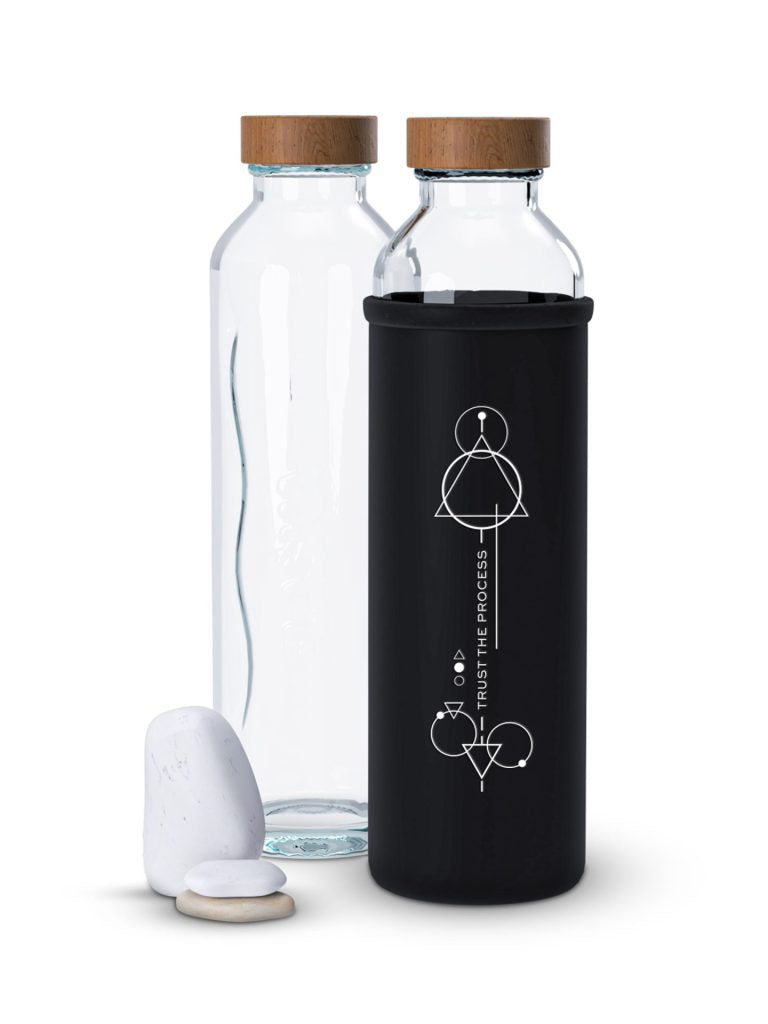 zwei glas trinkflaschen mit holzdeckeln eine hat eine schwarze hülle mit geometrischem design und dem text trust the process