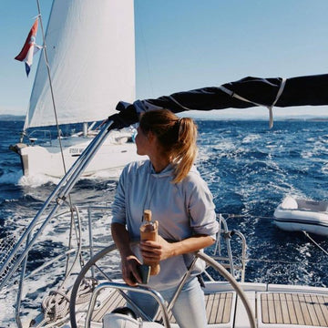 frau segelt auf einer yacht und hält eine wiederverwendbare flaska wasserflasche aus glas