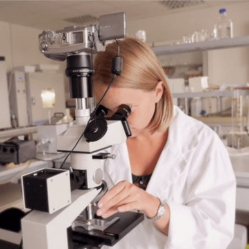 wissenschaftlerin im weißen kittel betrachtet proben im labor unter mikroskop
